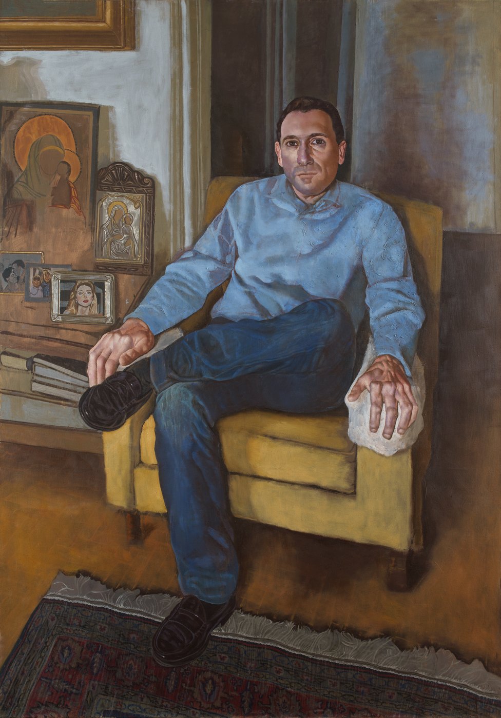 Aris Mertilis, Among the Icons (Ανάμεσα στις εικόνες), oil on canvas. Man in a pale blue shirt in a yellow armchair, icons and family photographs beside him.